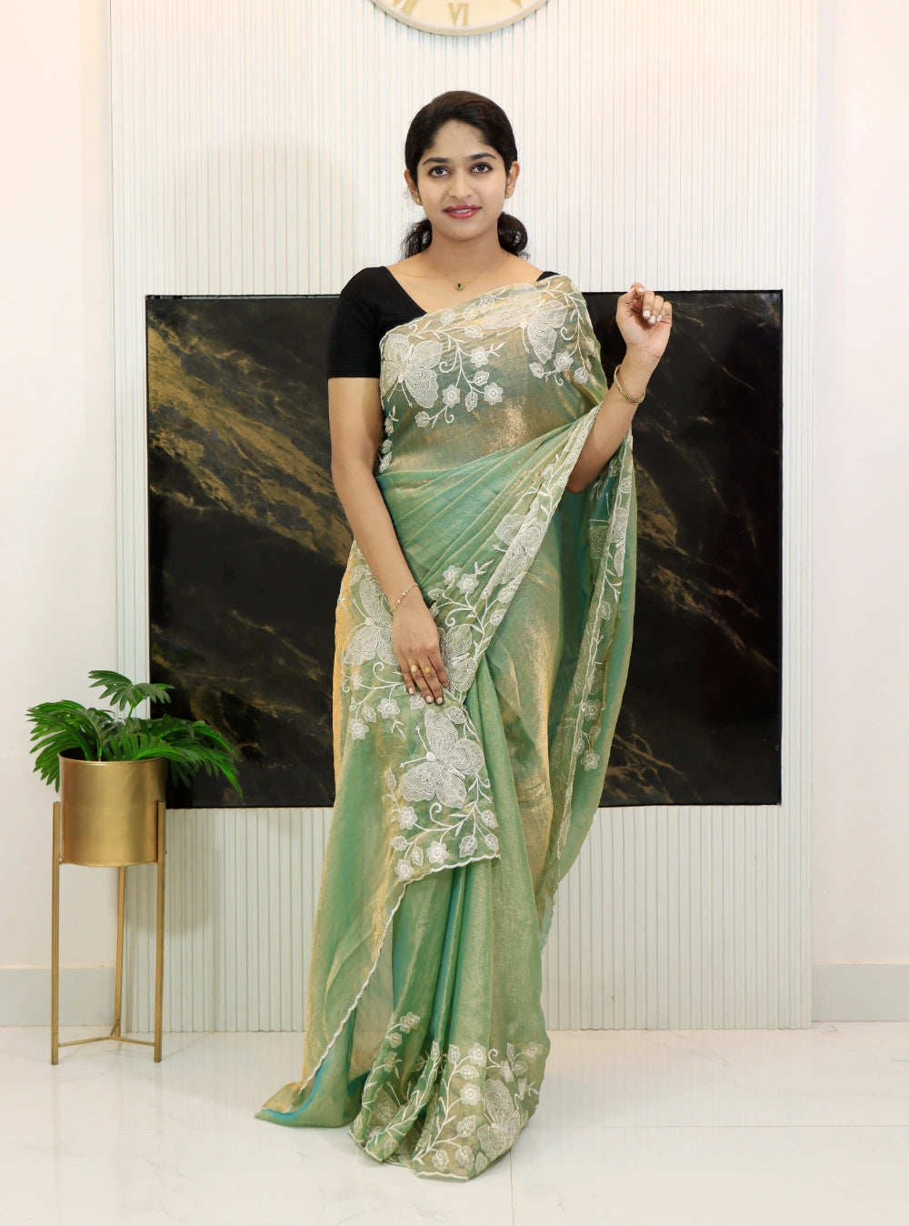 Woman wearing a green saree with a floral pattern in a minimalistic room.