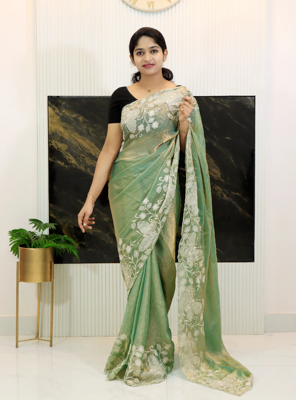 Woman wearing a green saree with white lace design indoors.