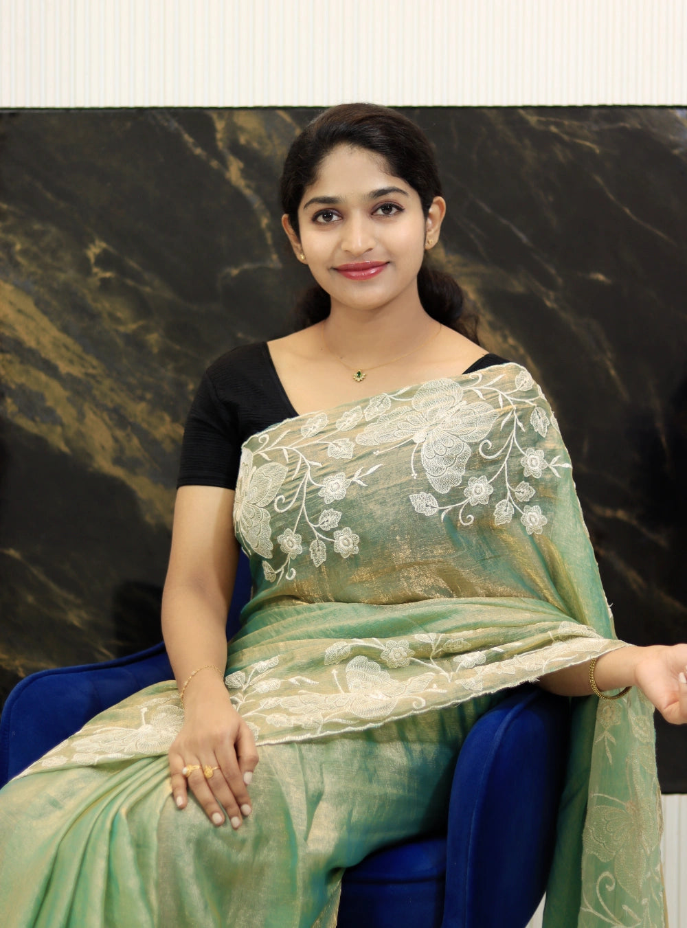 Woman wearing a green saree with white embroidery against a dark marble background