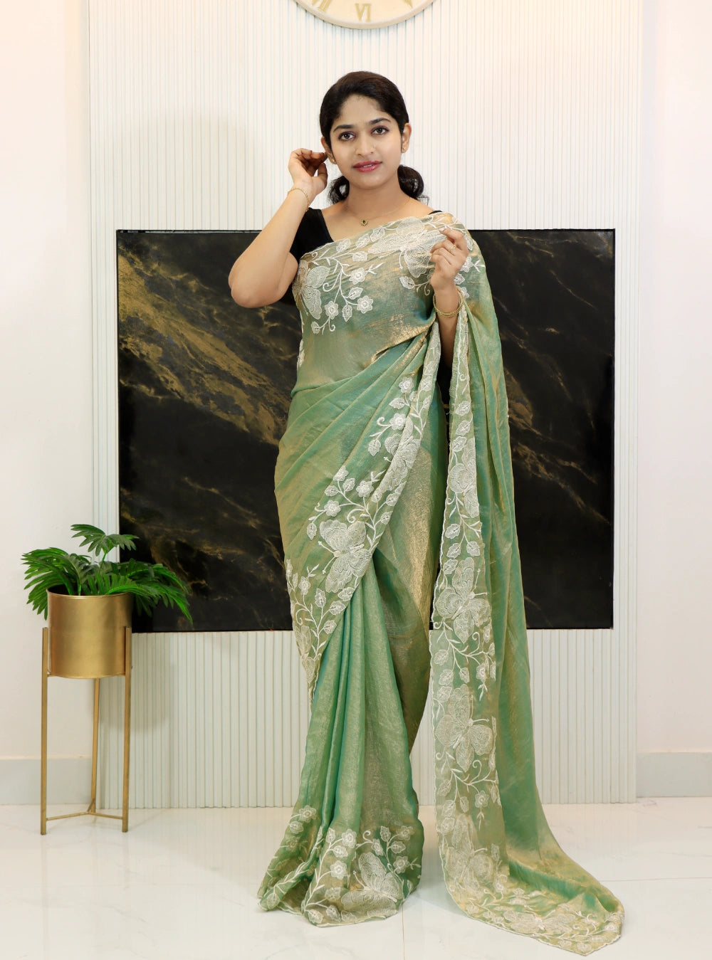 Woman wearing a green saree with a white blouse in a minimalistic room.